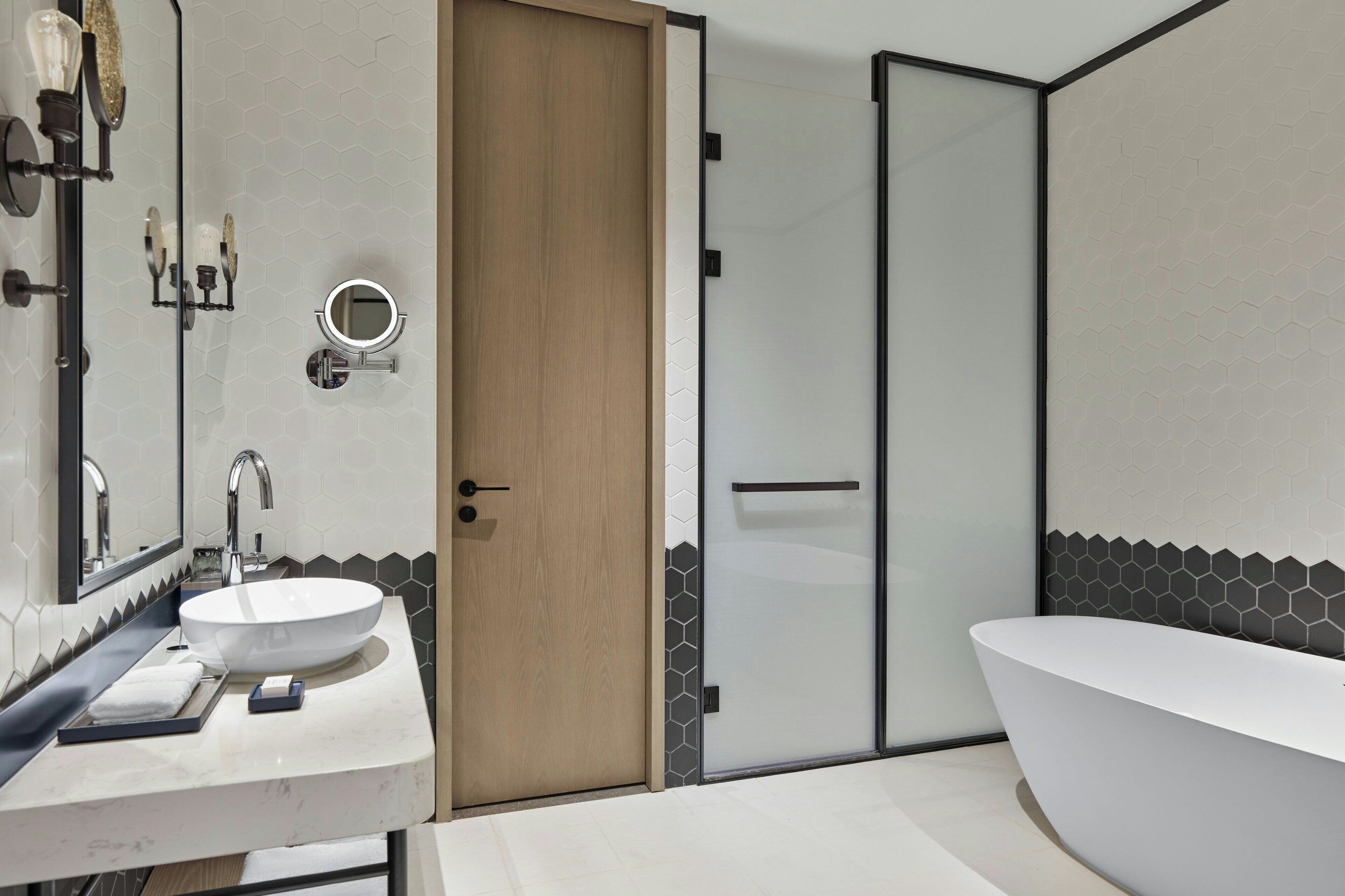A modern bathroom with a large white sink, a freestanding bathtub, and a wooden door.
