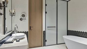 A modern bathroom with a large white sink, a freestanding bathtub, and a wooden door.