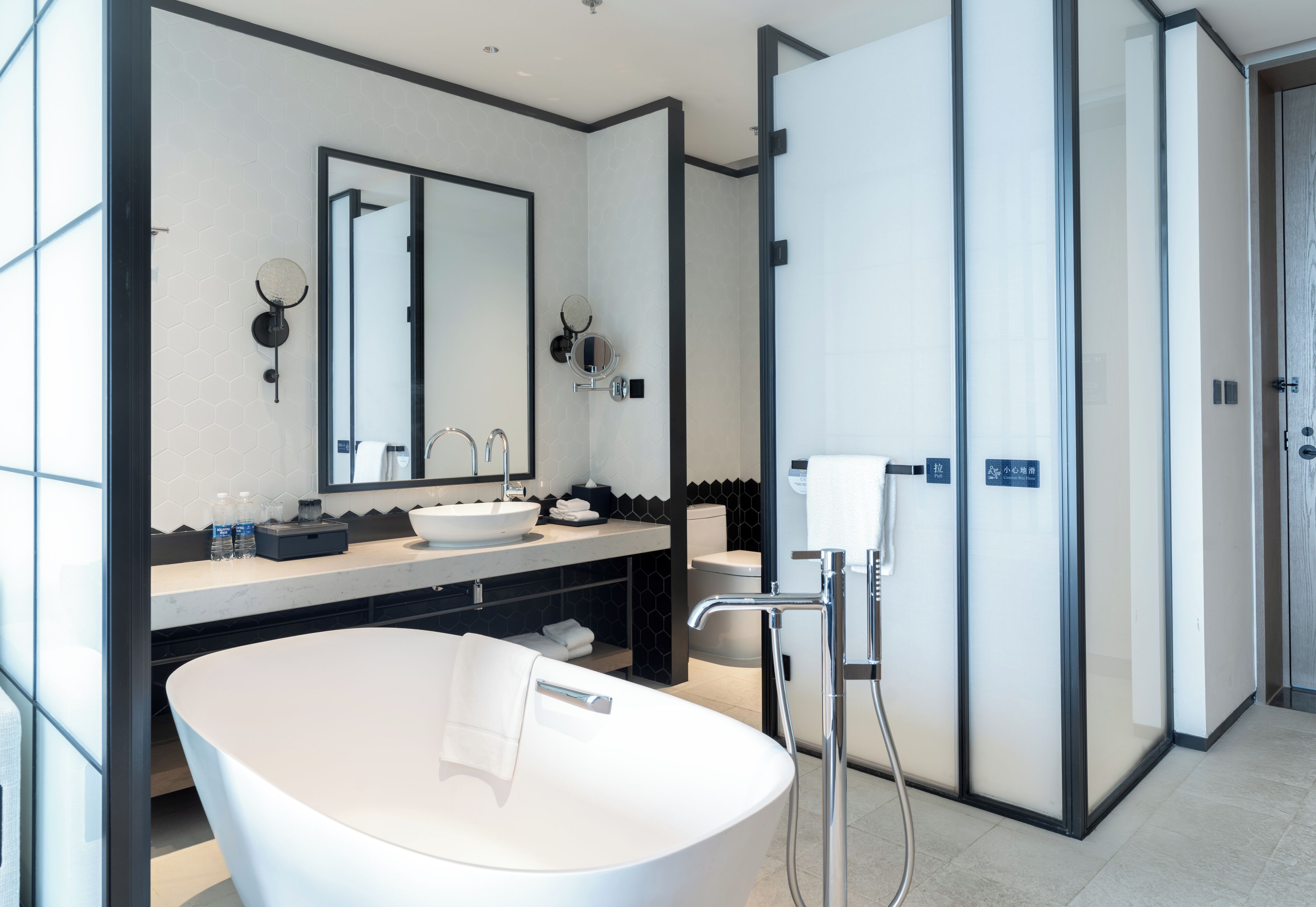 A modern bathroom with a freestanding bathtub, a large mirror, and a vanity with a sink and towel rack.