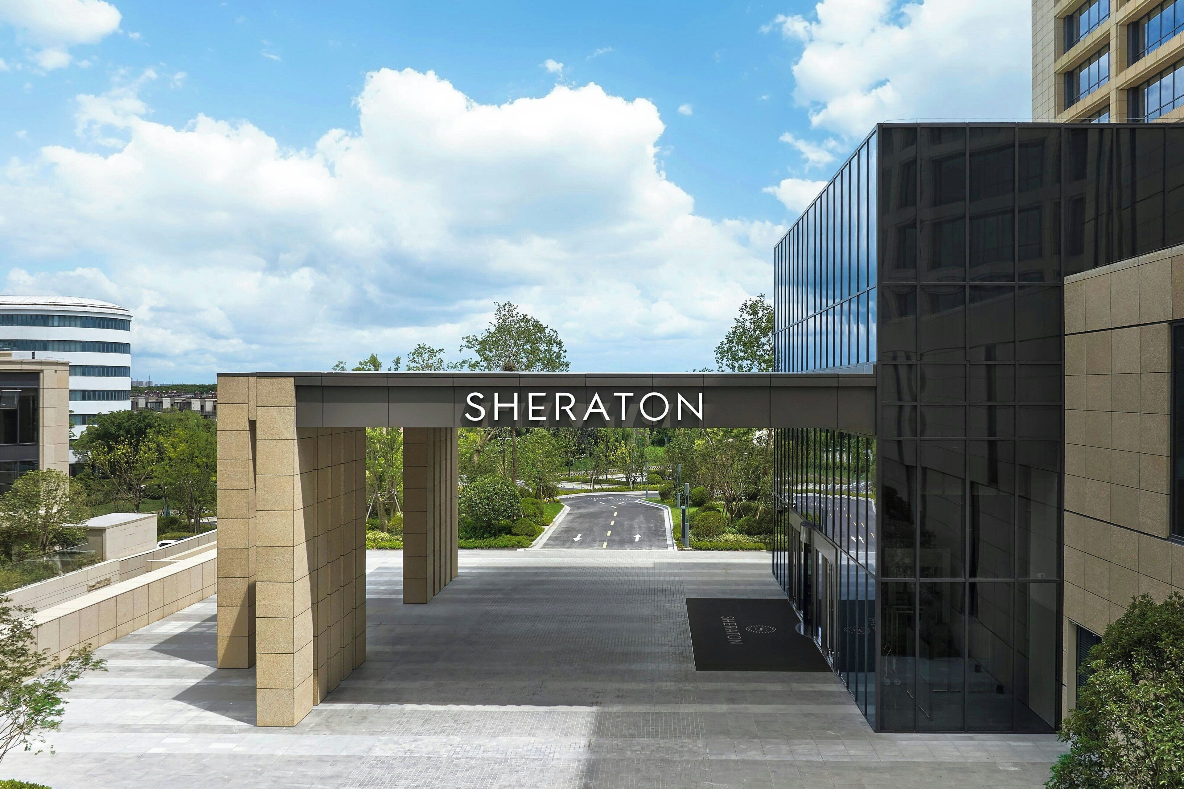 A hotel entrance with a sign reading "SHERATON" and a modern glass building to the right.