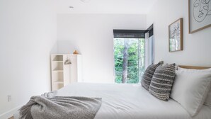 A bedroom with a large bed, a wooden headboard, a window with a view of trees, and a white wardrobe.