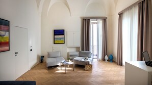 Ein modernes Wohnzimmer mit Sofa, Sessel und Couchtisch, einem Flachbildfernseher und einem großen Fenster mit Vorhängen.