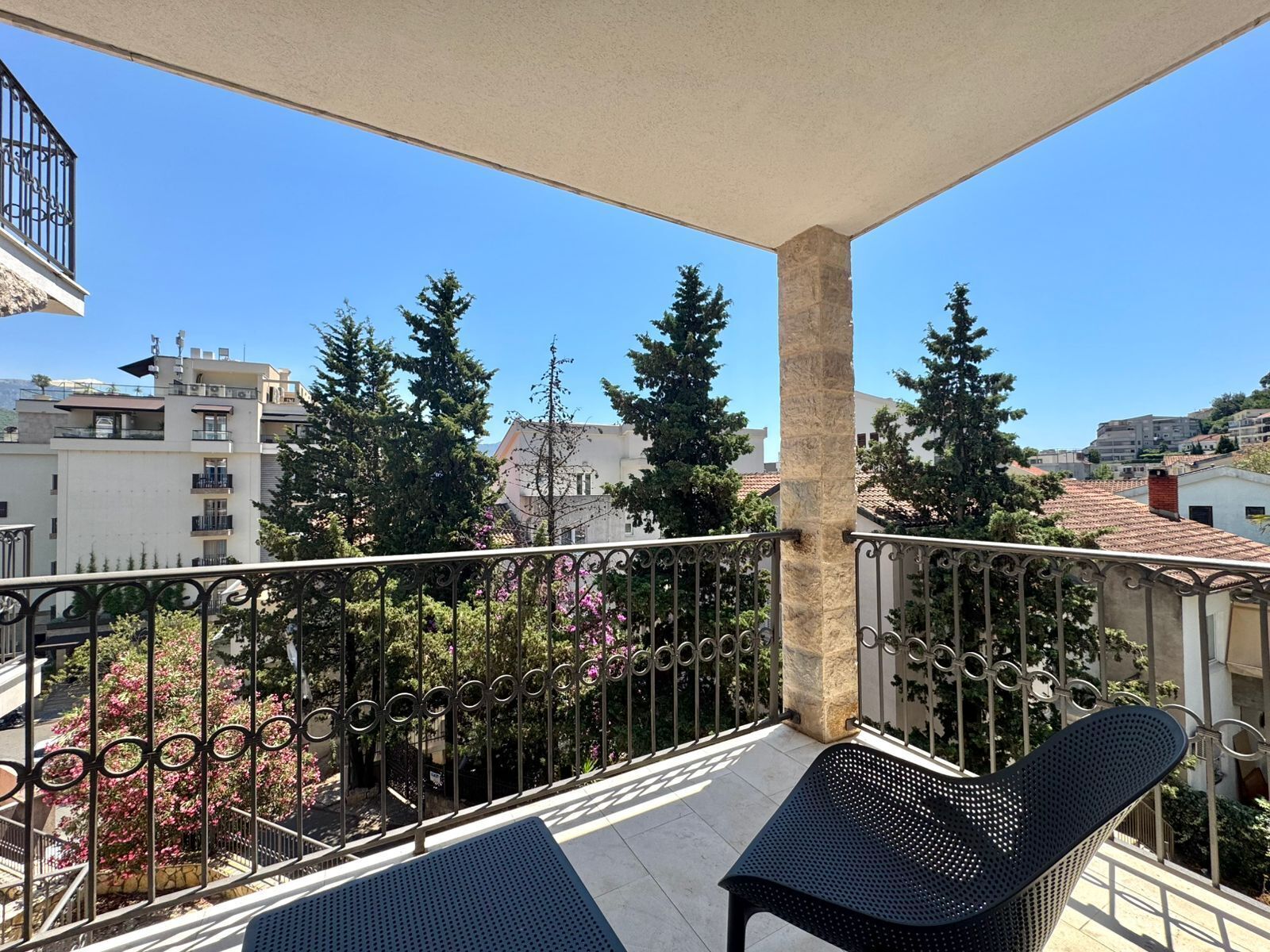 A balcony with a stone pillar, metal railing, and two black chairs.