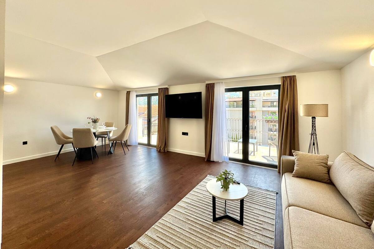 Un vaste espace de vie comprenant un canapé, une petite table et un téléviseur fixé au mur. Un balcon offre une vue sur la ville.