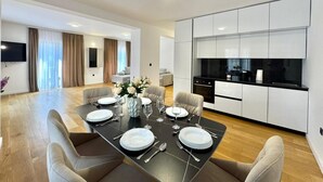 Un espace repas moderne avec une table noire dressée pour six personnes, entourée de chaises de couleur beige. Un vase contenant des fleurs blanches est posé sur la table.