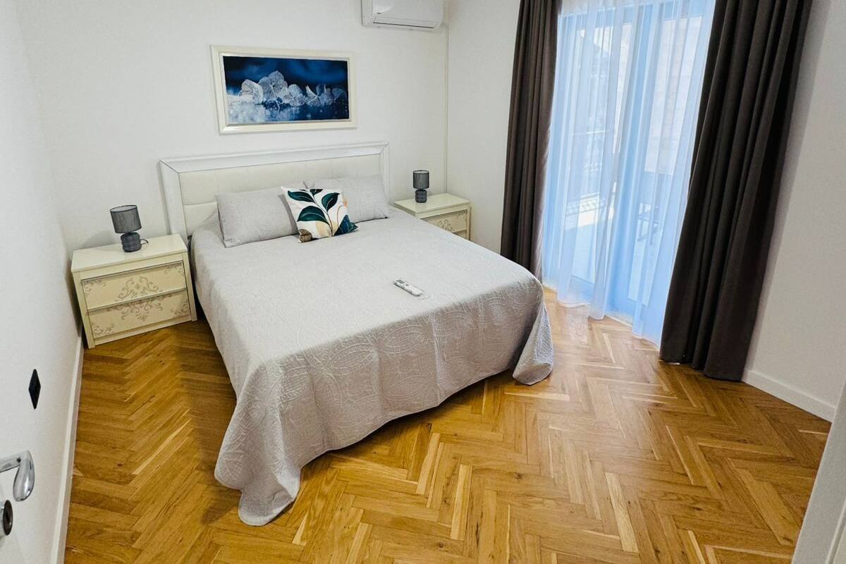 Une chambre d’hôtel avec un lit, des tables de chevet, un climatiseur, un tableau et une fenêtre avec des rideaux.