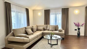Una sala moderna con un sofá seccional color beige, una mesa de centro redonda y un jarrón decorativo con flores.