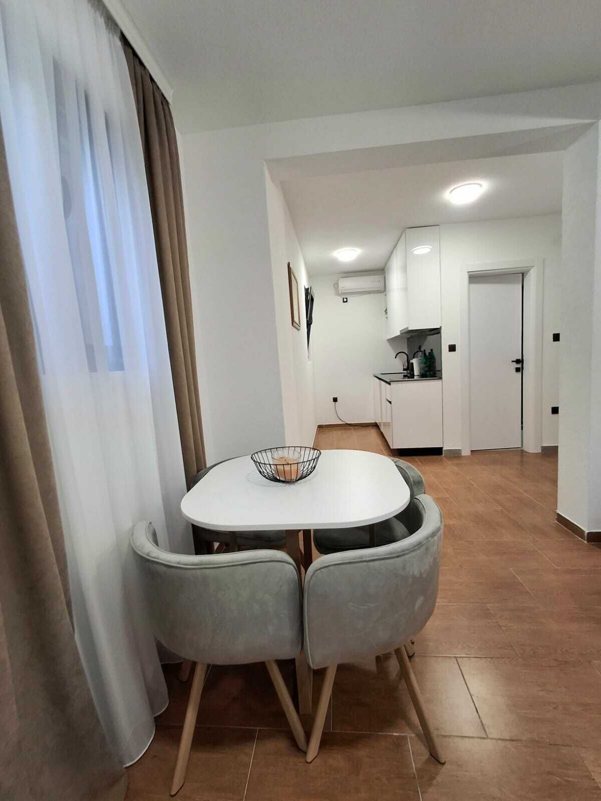 Una cocina moderna con armarios blancos y un comedor con una mesa redonda, dos sillas grises y un tazón de metal.