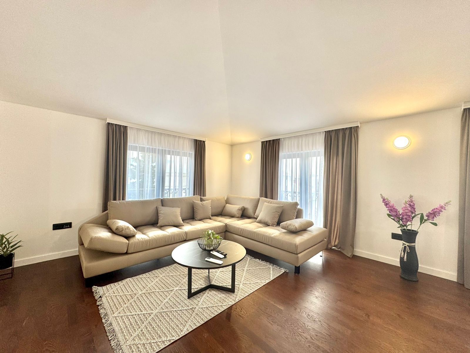 A modern living room with a beige sectional sofa, a round coffee table, and a potted plant.