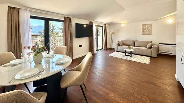 Un salon moderne avec un canapé, un téléviseur à écran plat et un coin repas avec une table dressée pour quatre personnes.