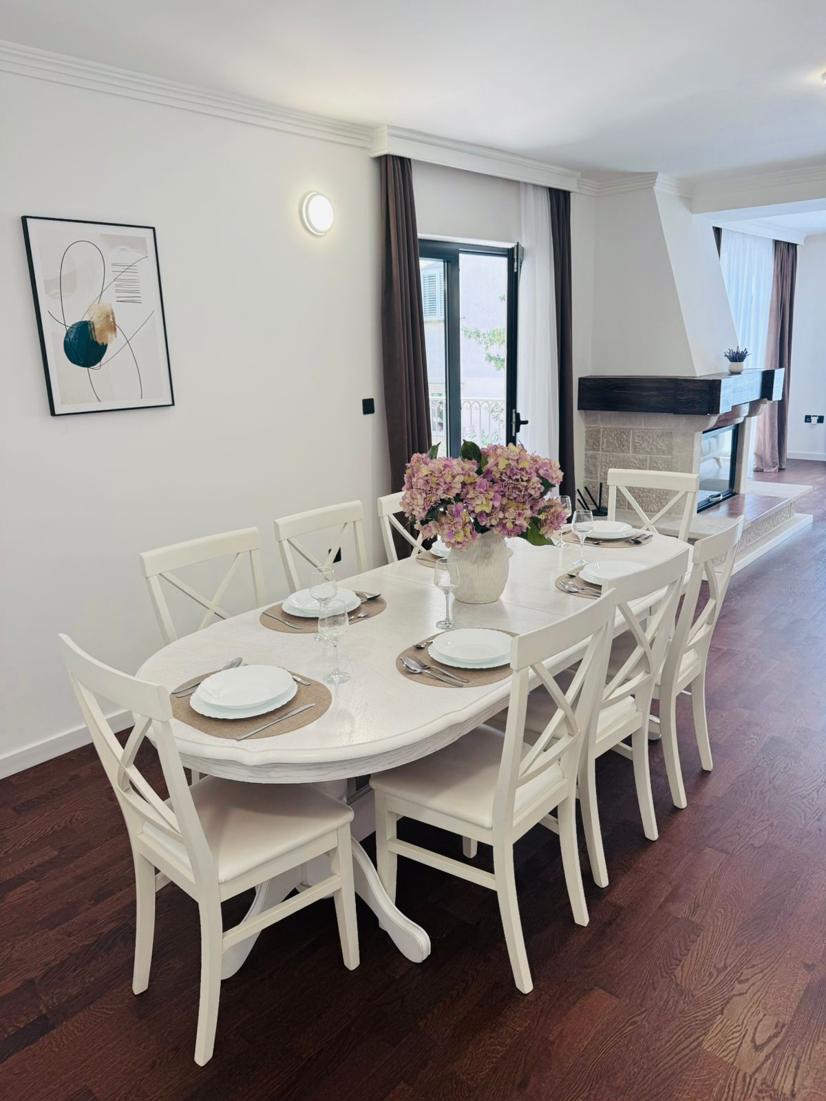 Un espace repas avec une table ronde blanche, dressée pour six personnes, entourée de chaises blanches.