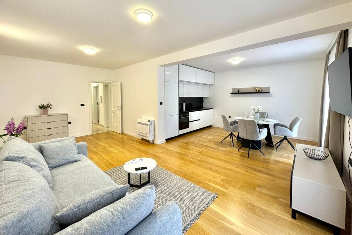 Un salon moderne avec un canapé gris, une petite table ronde et un coin repas comprenant une table blanche et des chaises grises.