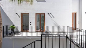Un edificio blanco con dos ventanas y una puerta, un balcón con barandilla y una palmera.