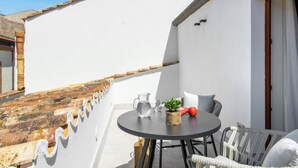 Un balcón con una mesa redonda, sillas, una planta en maceta, una jarrón y un vaso.
