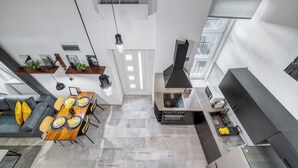 Een moderne keuken met een inbouwfornuis, een zithoek met een houten tafel en stoelen, en een grijze bank met gele kussens.