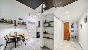 Een moderne eetruimte met een houten tafel en stoelen, een zwarte hanglamp en wandplanken met decoratieve objecten.