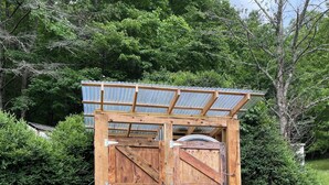 A wooden structure with a metal roof, possibly a storage shed or small building, surrounded by greenery.