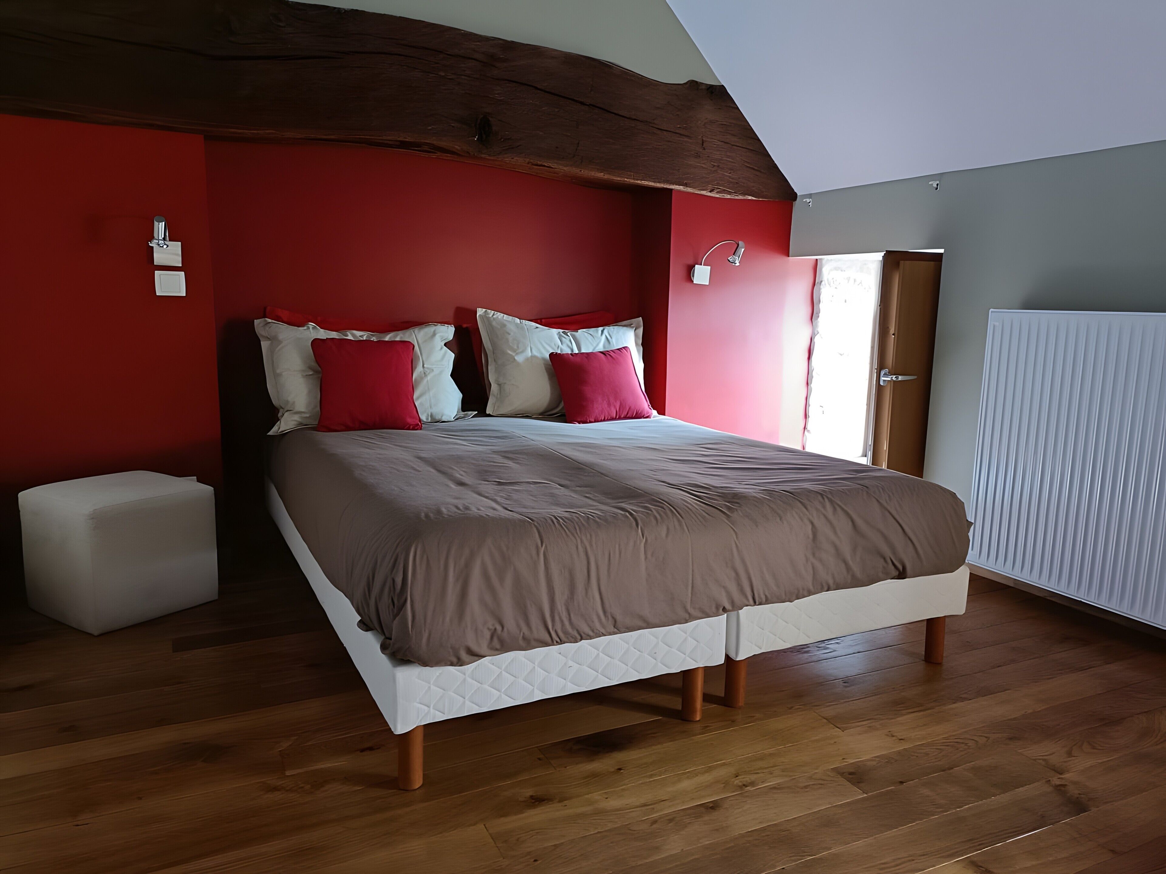 Een slaapkamer met een bed, houten vloer, rode muren en een schuin dak.