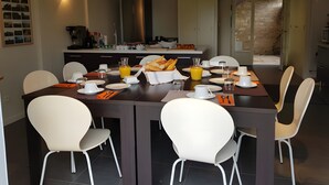 A dining area with a long table, white chairs, and a kitchen in the background. - Guest Room "Chambre Chocolat" with Shared Pool, Shared Terrace and Wi-Fi (Beaumont sur Grosne)