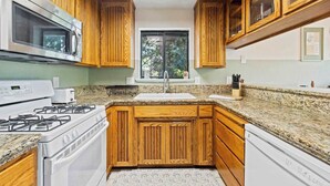 Cucina con mobili in legno, piano di lavoro in granito, forno a microonde integrato, fornello e finestra vista alberi.