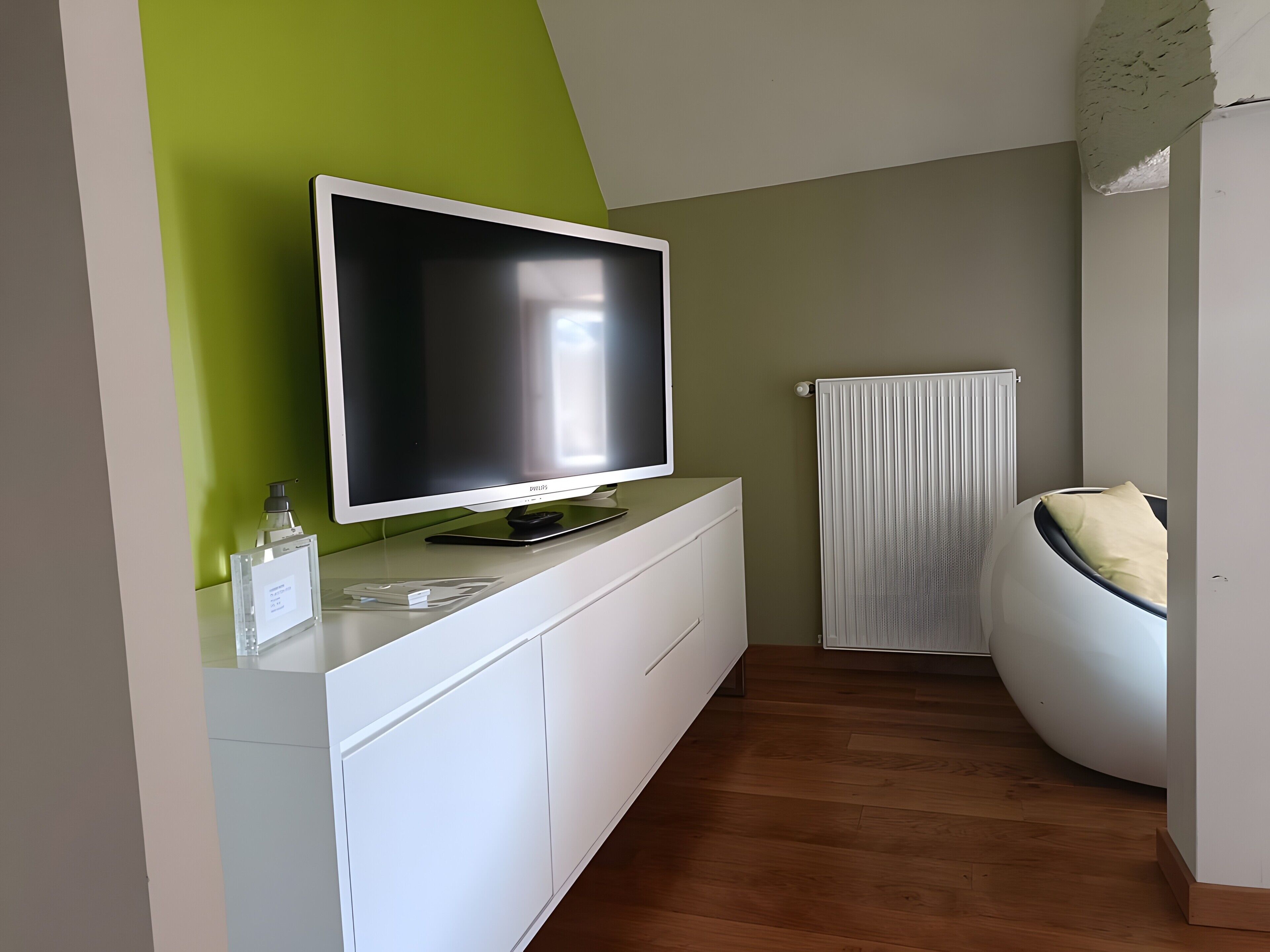 Une chambre moderne avec un téléviseur à écran plat posé sur un meuble blanc, un radiateur et un lit au design incurvé original.