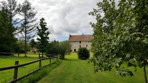 A grassy area with a wooden fence, trees, and a building with a tiled roof in the background. - Guest Room 'Tilleul' with Shared Pool, Shared Terrace and Wi-Fi (Beaumont sur Grosne)