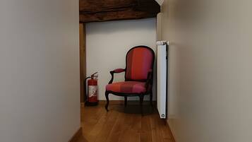 Un escalier étroit mène à une pièce où se trouvent un fauteuil rouge, des poutres en bois et un extincteur.
