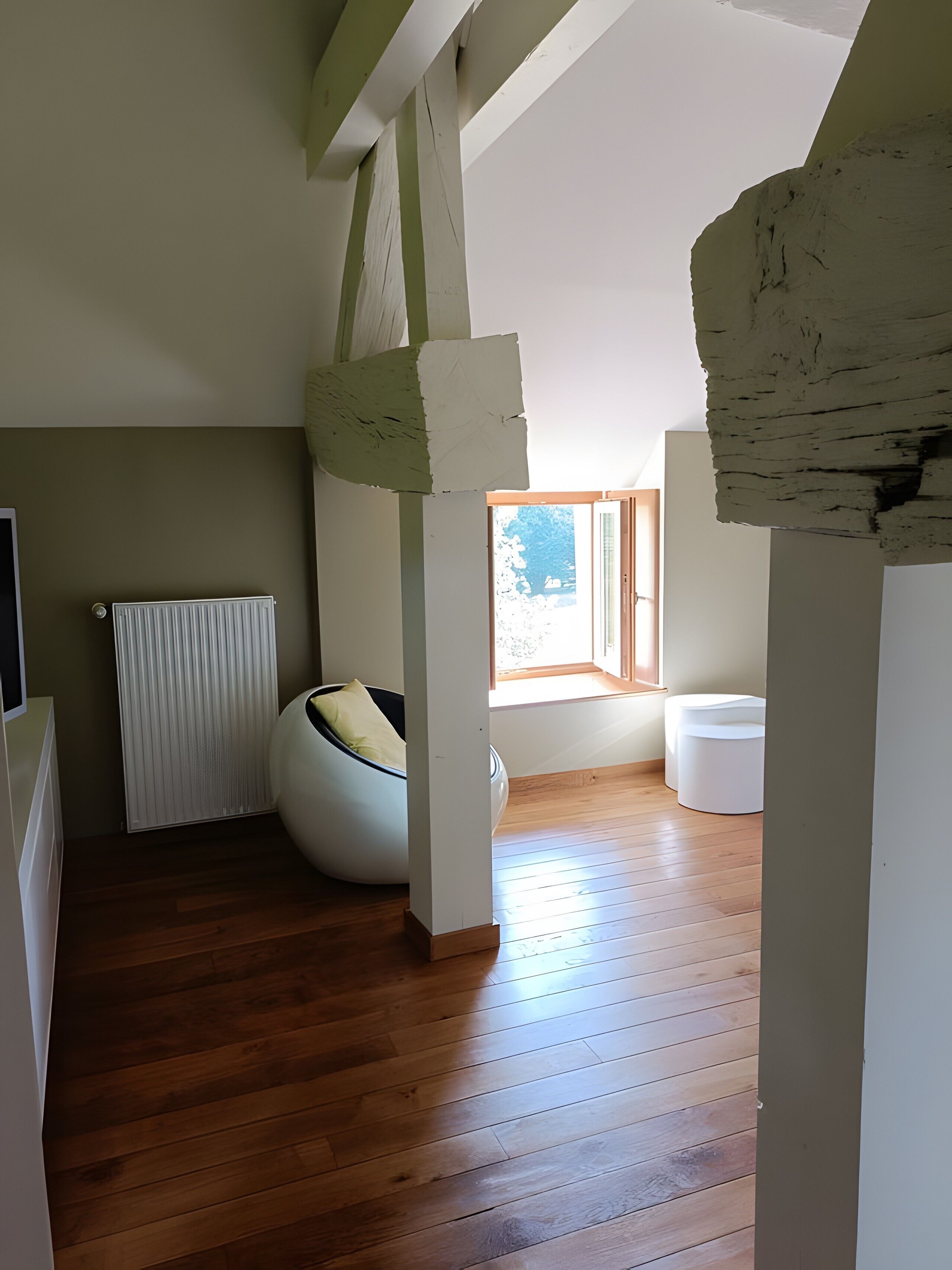 A room with wooden flooring, a white radiator, a white chair, and a window with a view.