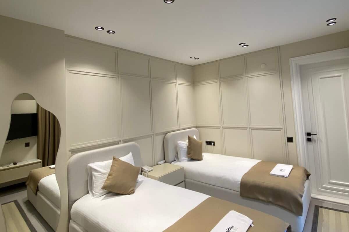 A hotel room with two beds, a mirror, a TV, and recessed ceiling lights.