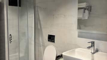 Un baño moderno con cabina de ducha de vidrio, inodoro blanco, espejo grande y lavamanos con encimera de vidrio.