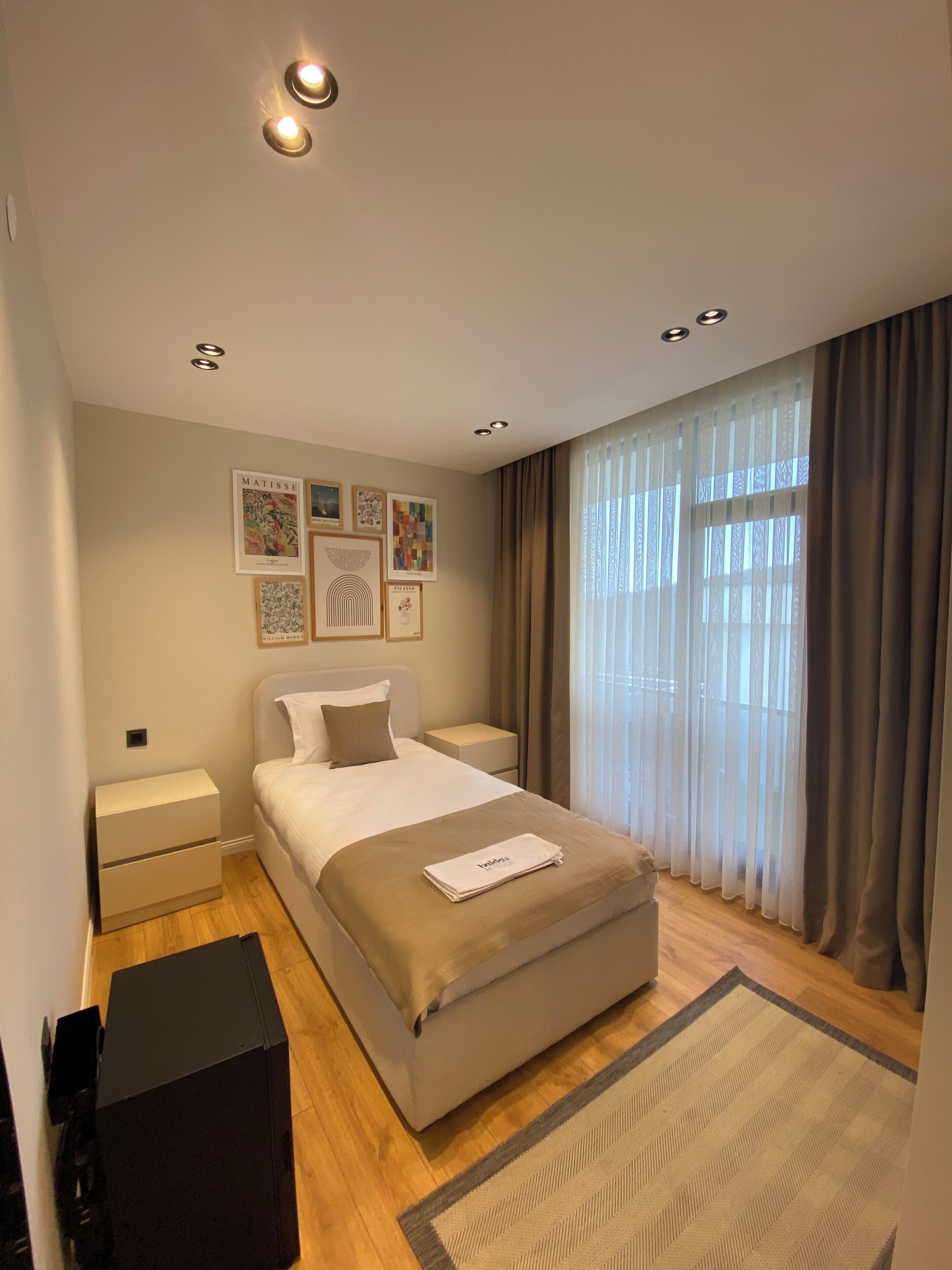 Una habitación de hotel moderna con una cama grande, mesitas de noche, un escritorio y obras de arte en las paredes.