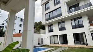 A modern multi-story residential building with balconies, a swimming pool, and a well-maintained lawn. - Bakku House (Atakum)