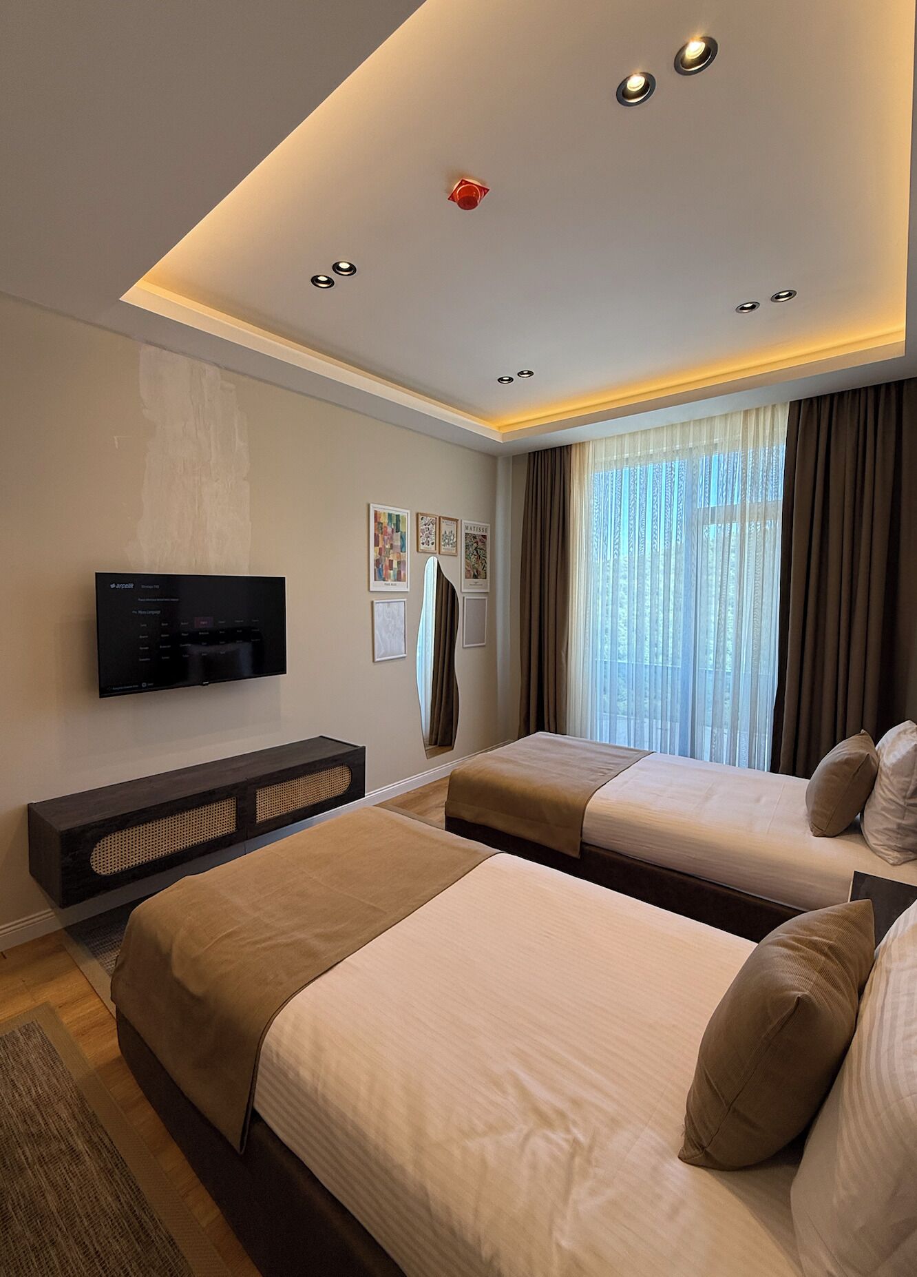 Una habitación de hotel moderna con dos camas, un televisor de pantalla plana, una mesita de consola y un ventanal grande con cortinas.