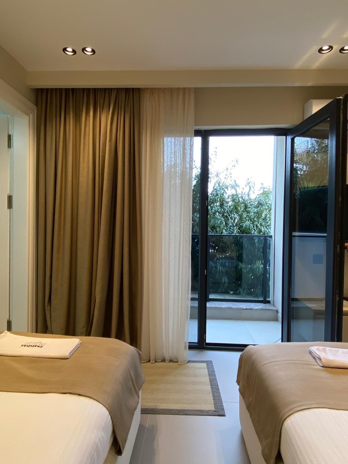 Habitación de hotel con dos camas, una puerta corredera de vidrio a un balcón y vista a zonas verdes.
