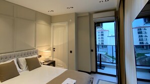 A hotel room with a large bed, a bedside table with a lamp, a door, and a view of the outside. - Bakku House (Atakum)