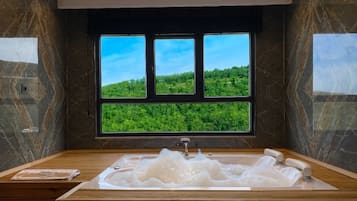 Un baño moderno con una bañera grande, un tocador de madera y un ventanal con vistas a un paisaje verde.