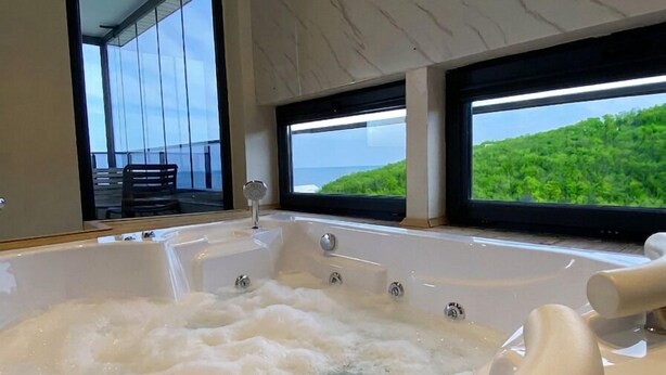 A modern bathroom with a large bathtub, a view of the ocean, and a balcony with outdoor furniture. - Bakku House (Atakum)