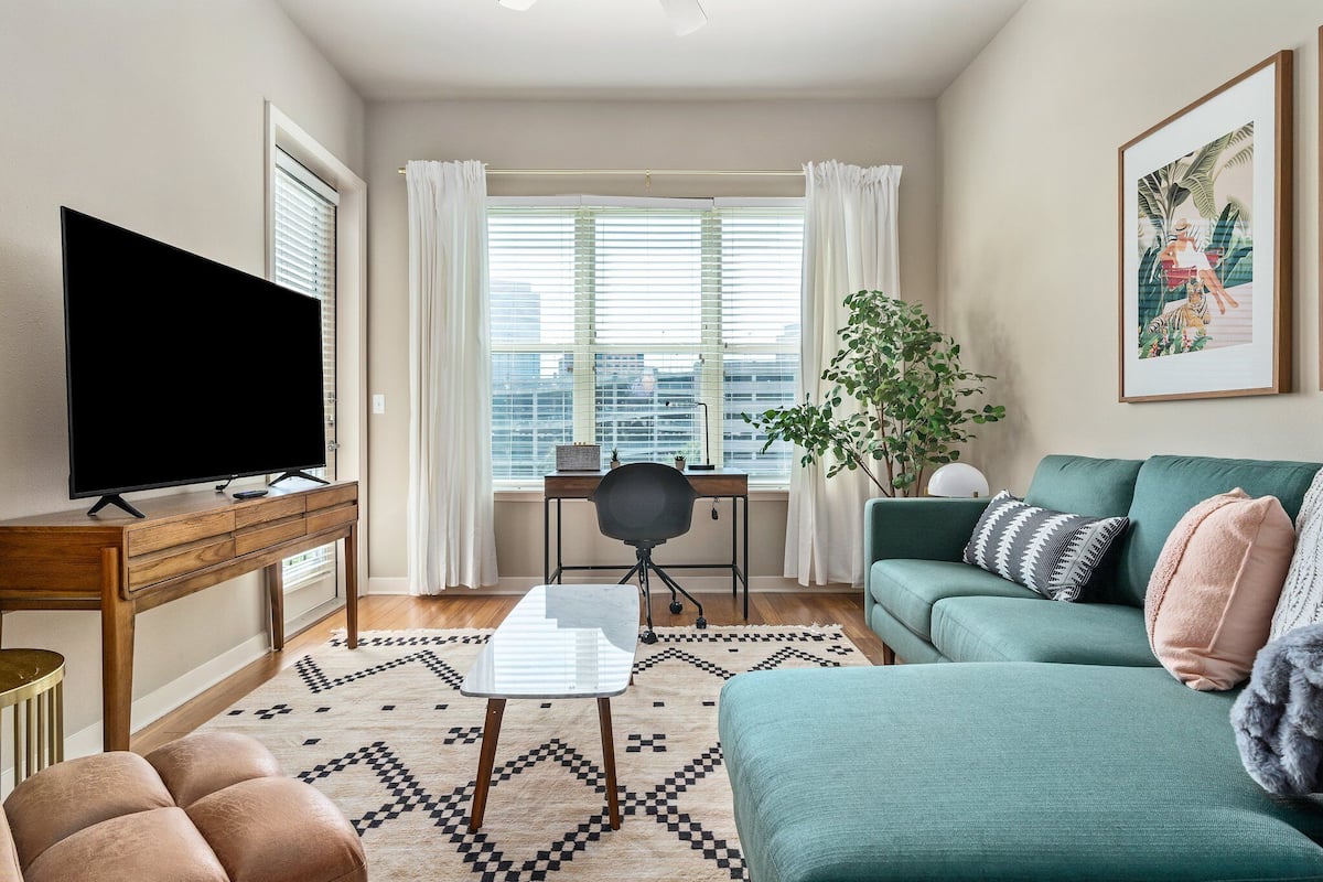 A modern living room with a large flat-screen TV, a green sofa, a coffee table, and a desk with a chair.