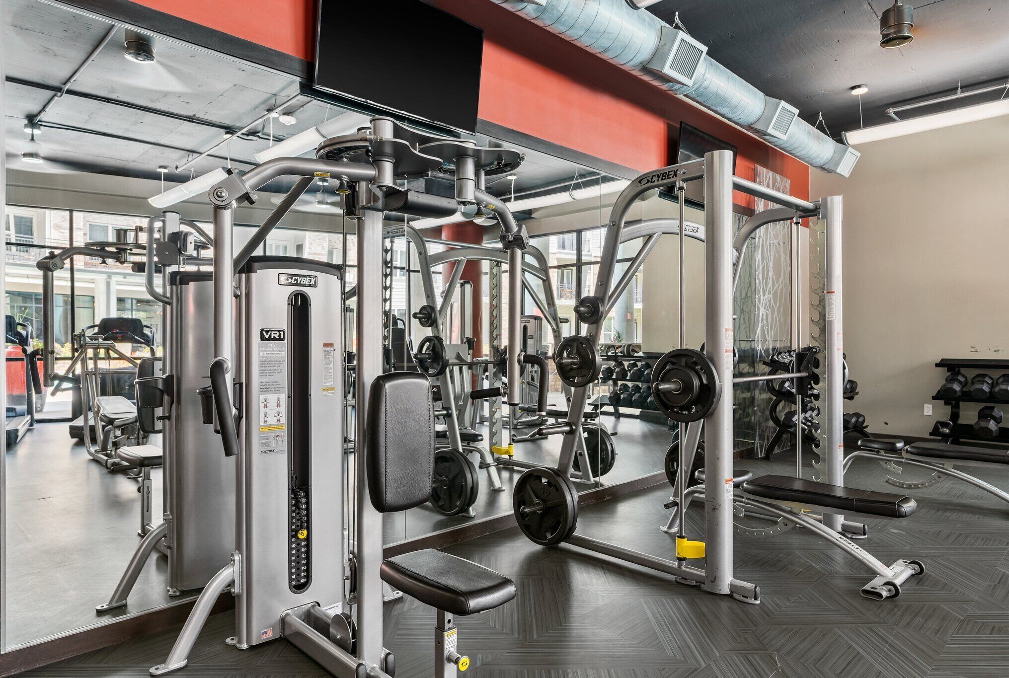Ett gym med olika träningsmaskiner, speglar och utrustning för styrketräning.