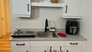 A modern kitchen with white cabinets, a stainless steel sink, a coffee maker, and a small shelf with decorative items.