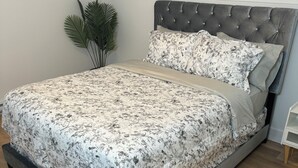 A modern bedroom with a large bed, a grey upholstered headboard, and a framed landscape painting above the bed.