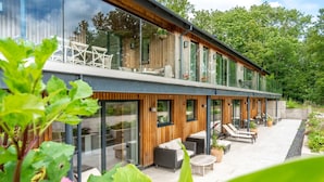 A modern house with large glass windows, outdoor seating, and a garden area. - Gamekeeper's Lodge - sleeps 8 guests  in 4 bedrooms (Stratford-upon-Avon)