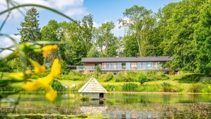 A lakeside cabin with a wooden deck, surrounded by lush greenery and a small dock. - Gamekeeper's Lodge - sleeps 8 guests  in 4 bedrooms (Stratford-upon-Avon)