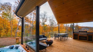 A wooden deck with a hot tub, a fire pit, and a barbecue grill, overlooking a forest with autumn foliage. - Berghaus 8 - 15mins away from Mont-Tremblant! (Lac-Supérieur)