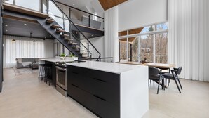 A modern kitchen with a central island, black cabinetry, and a wooden staircase. - Berghaus 8 - 15mins away from Mont-Tremblant! (Lac-Supérieur)