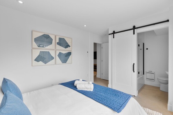 A modern bedroom with a bed, blue pillows, a blue throw blanket, and geometric wall art.