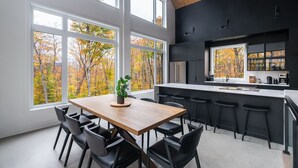 A modern kitchen with large windows, a dining area with a wooden table and chairs, and a black and white color scheme. - Berghaus 8 - 15mins away from Mont-Tremblant! (Lac-Supérieur)