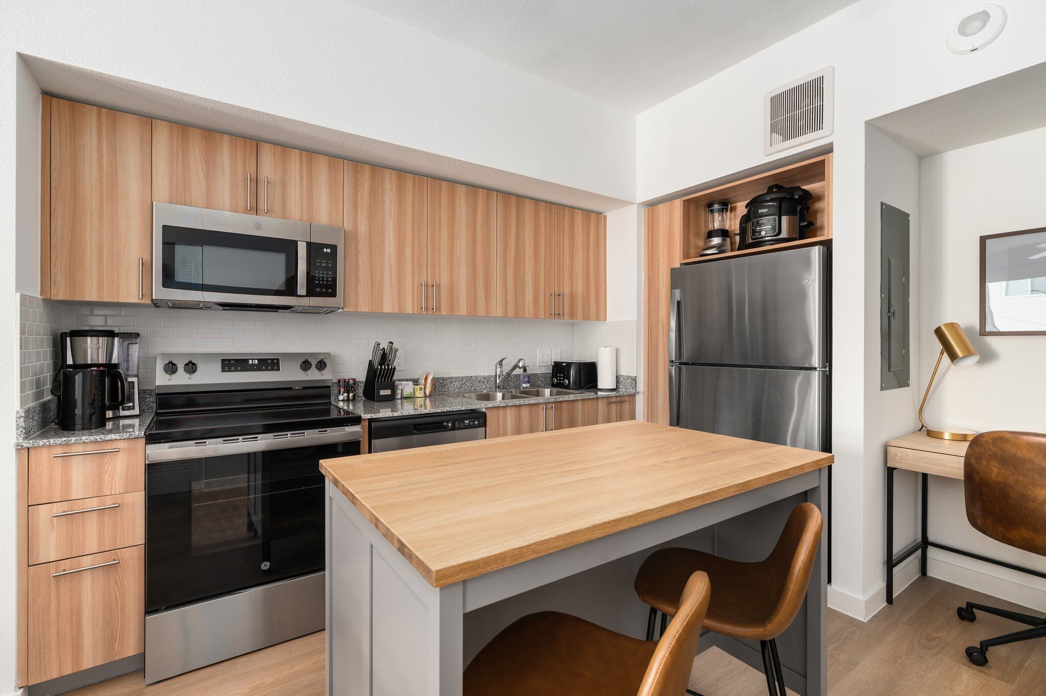 A compact kitchen with wooden cabinets, stainless steel appliances, a built-in microwave, and a small island with seating.