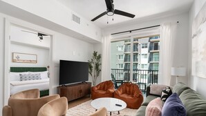 Un soggiorno moderno con una televisione a schermo piatto, divani in pelle, un tavolino rotondo e un balcone con vista sulla città.