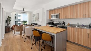 Una cucina moderna con mobili in legno, un'isola centrale con sgabelli da bar e un'area pranzo con vista sull'esterno.